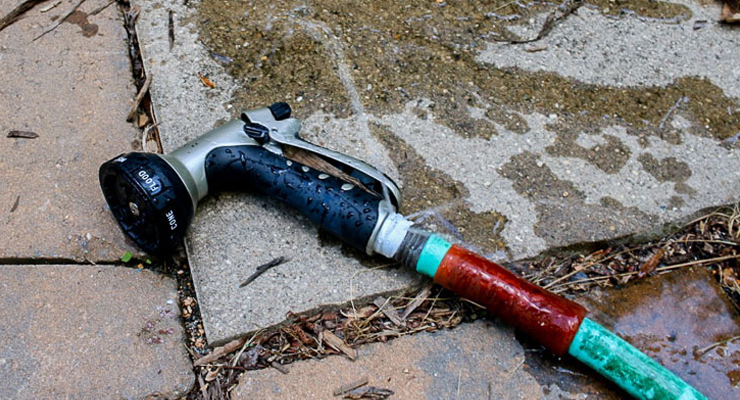 Vandslange med justerbart sprayhoved liggende på flisebelægning – klar til brug i haven.