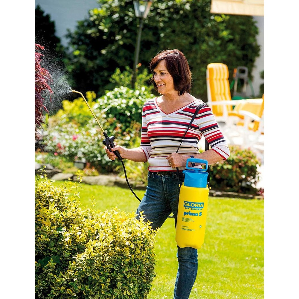 Kvinde vander buske med Gloria tryksprøjte i forhave