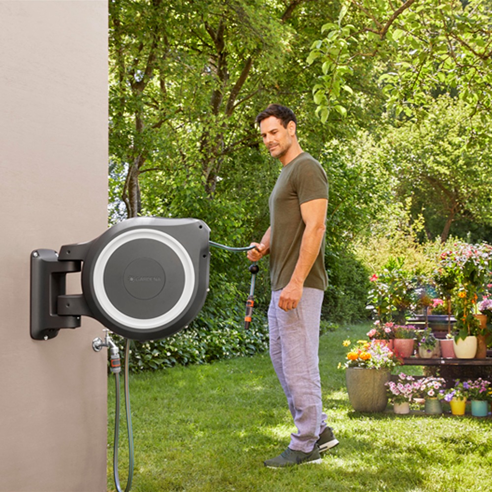 Gardena RollUp XL 30m slangeopruller monteret på en trævæg, fuldt udrullet med en mand, der vander haven.